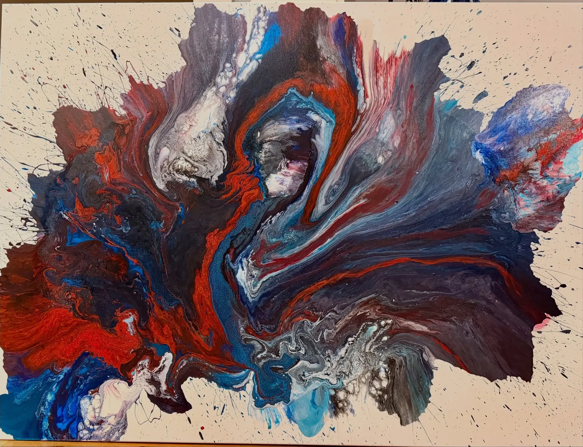 An abstract poured painting with swirls of red, navy, sky blue and white spreading across a white canvas, edged with small spatters.