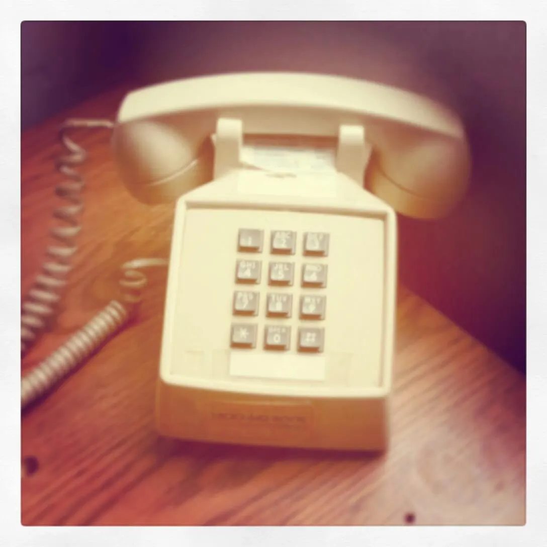 A cream push-button desk telephone on a wooden table, photographed with a soft, faded tint.
